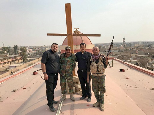 Fr. Ammar, another priest and two soldiers stand by a newly erected cross on the roof of Tahira church (church of the Immaculate, Syriac Catholic) in Qaraqosh, a Christian village liberated from IS.