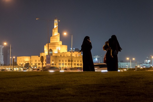 Two women, one carrying a child, wait for a car to pick them up in Doha, Qatar.