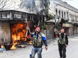 Turkish-backed Syrian rebels walk past a burning shop in Afrin on 18 March. (Photo: BULENT KILIC/AFP/Getty Images)