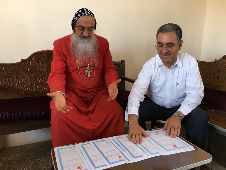 Syriac Orthodox Archbishop Samuel Aktas (in red) and Mor Gabriel Foundation Chairman Kuryakos Ergun welcome the returned property deeds from the Turkish Treasury. (Mor Gabriel Foundation)