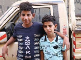 Marco (l) and Mina (r)standing next to the car that their father drove when he was killed. (Photo: World Watch Monitor)